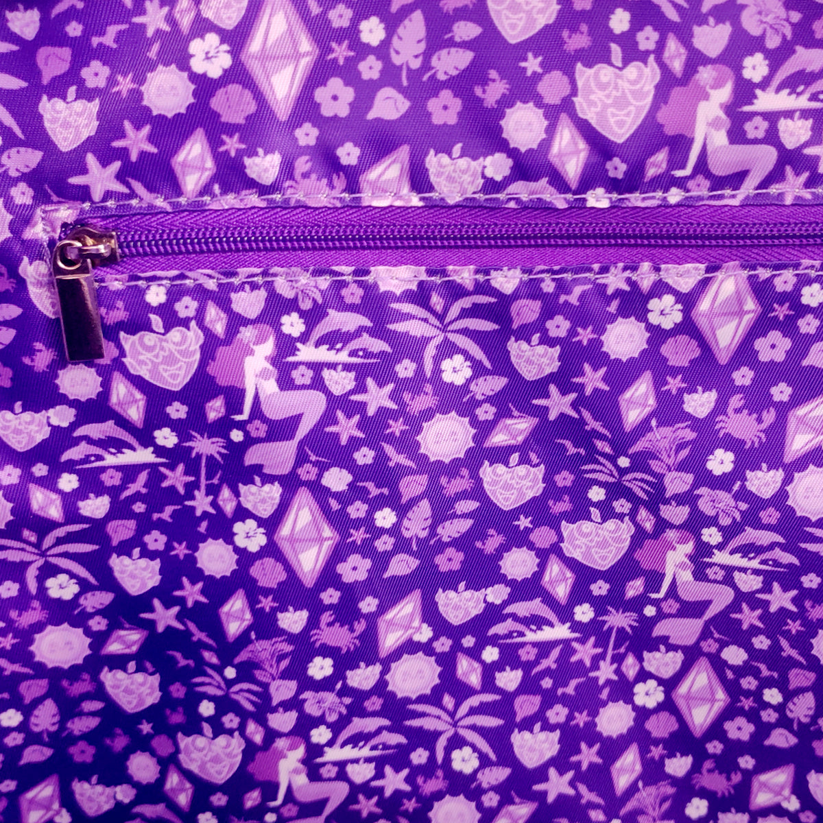 Close-up of a purple fabric item with an allover light purple pattern of flowers, stars, palm trees, and geometric shapes, featuring a matching purple zipper.