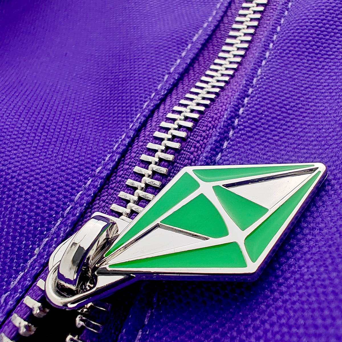 Close-up of a purple textured fabric zipper with a distinctive green and silver geometric pull tab.