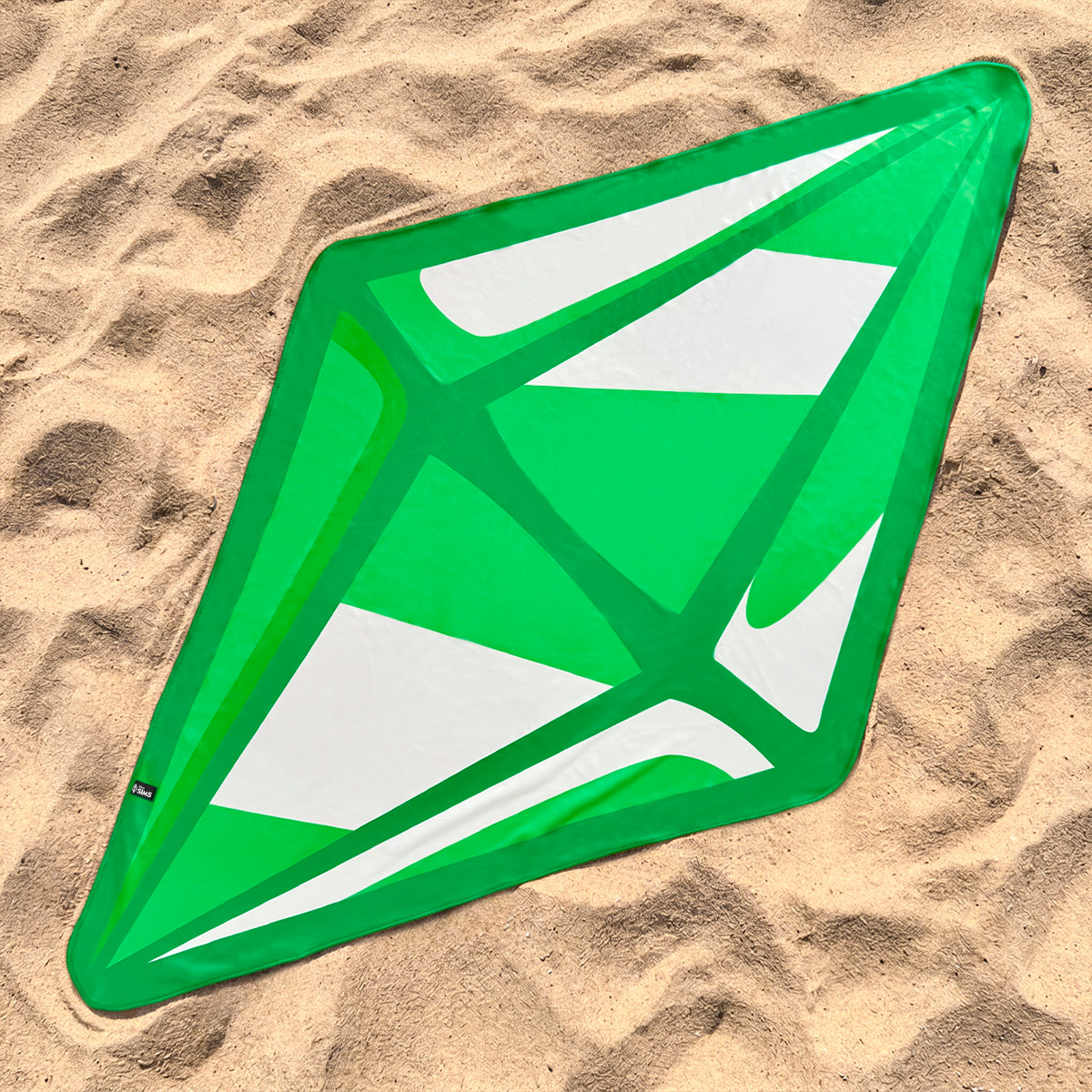 A green and white diamond-shaped beach towel laid flat on sandy beach ground.
