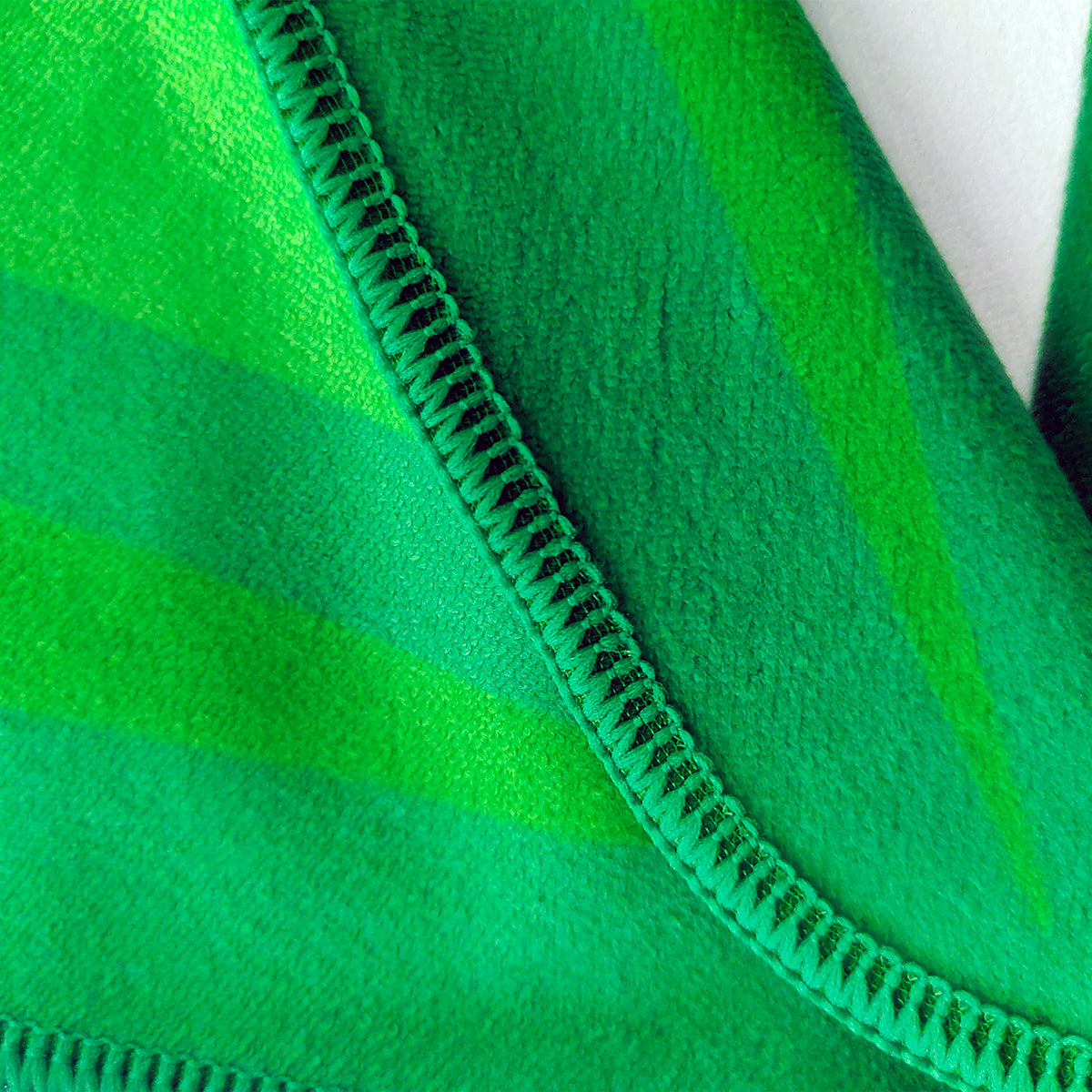 Close-up of a green fleece blanket with diagonal stripes in different shades of green and a visible stitched edge.