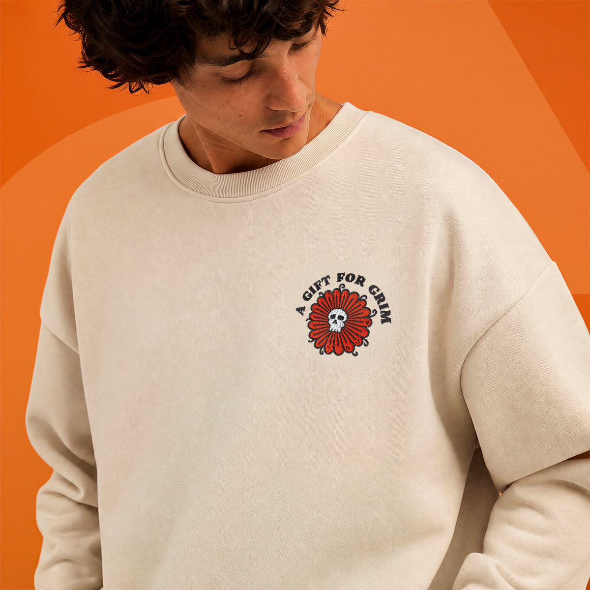 A close-up of a person wearing a cream-colored crewneck sweatshirt with a red and black graphic on the left chest that reads 'A GIFT FOR CRAZY'. The background is a solid orange color.