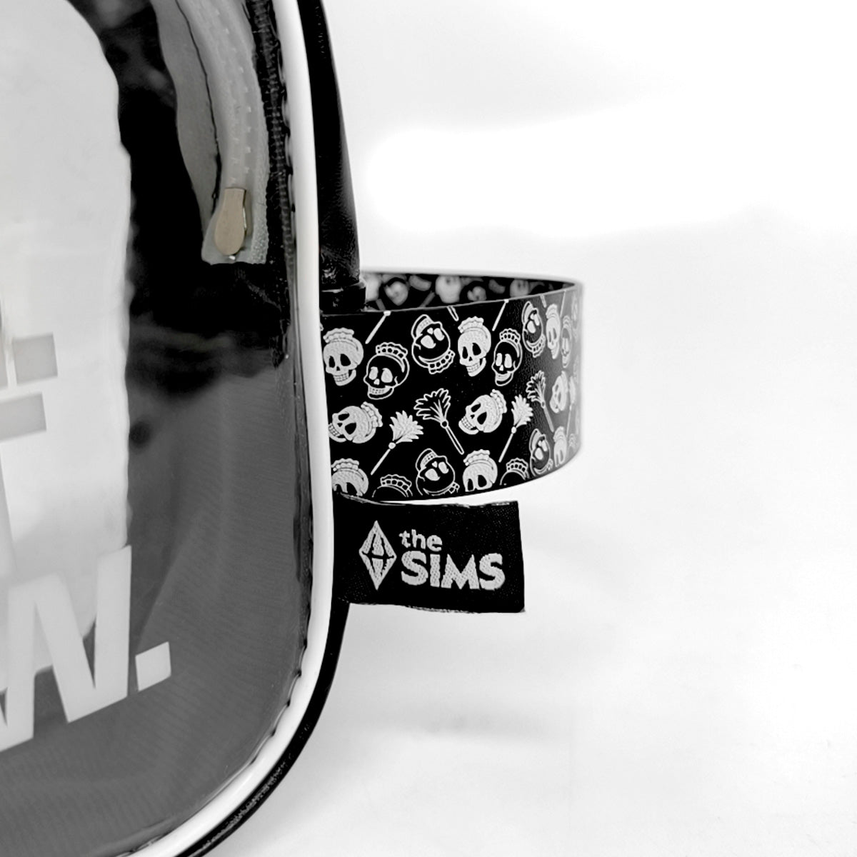 A close-up of a black and white patterned wrist strap attached to a clear vinyl bag, featuring a 'the SIMS' brand patch and skull motifs on a white background.