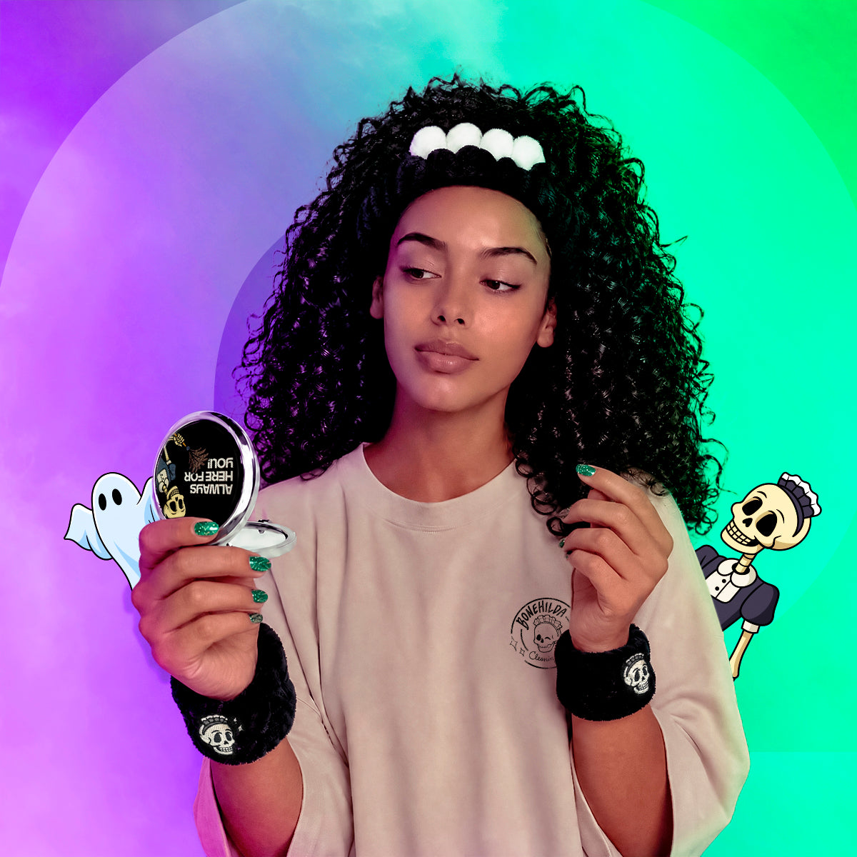 A woman with curly black hair wearing a black and white ghost-themed headband, a beige t-shirt, and black wristbands holds a small round sticker that reads 'FOR BURNER STRENGTH' with a ghost illustration. The background is a vibrant, circular gradient of purple, green, and blue with cartoon skeleton graphics on the sides.