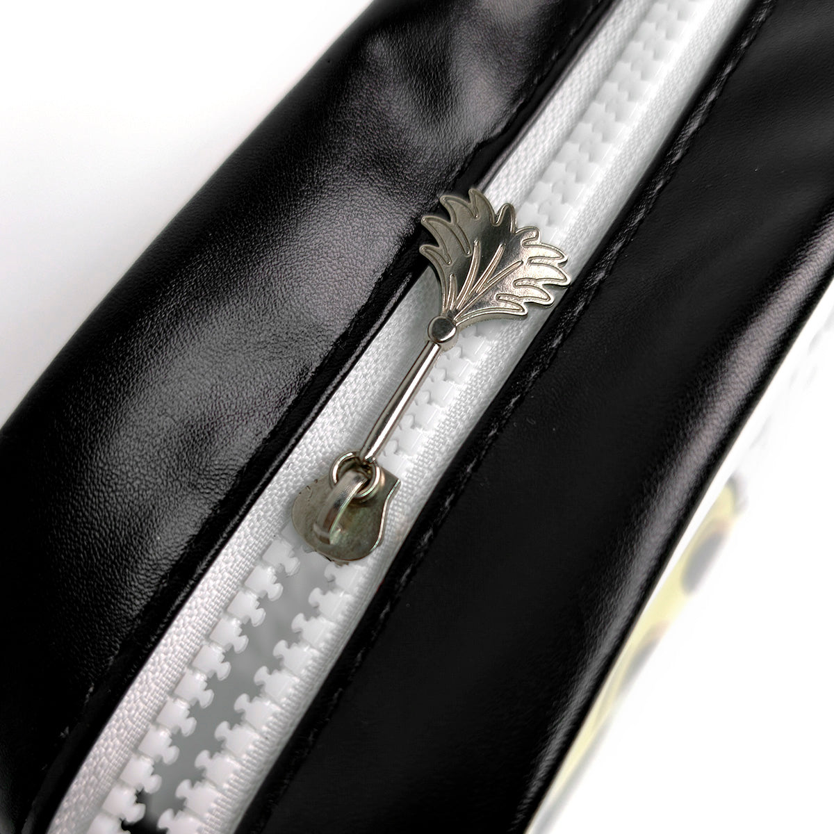 Close-up of a black faux-leather zipper pouch with a white zipper track and a silver metal pull tab shaped like a leaf.
