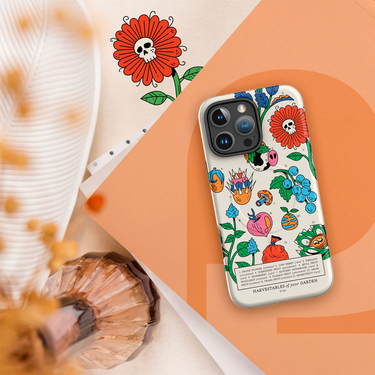 A phone case with a colorful 'Harvest Fakes @ Our Gardens' illustration print, shown on a white phone. The case is styled in a flat-lay composition on a peach and cream background with decorative props.