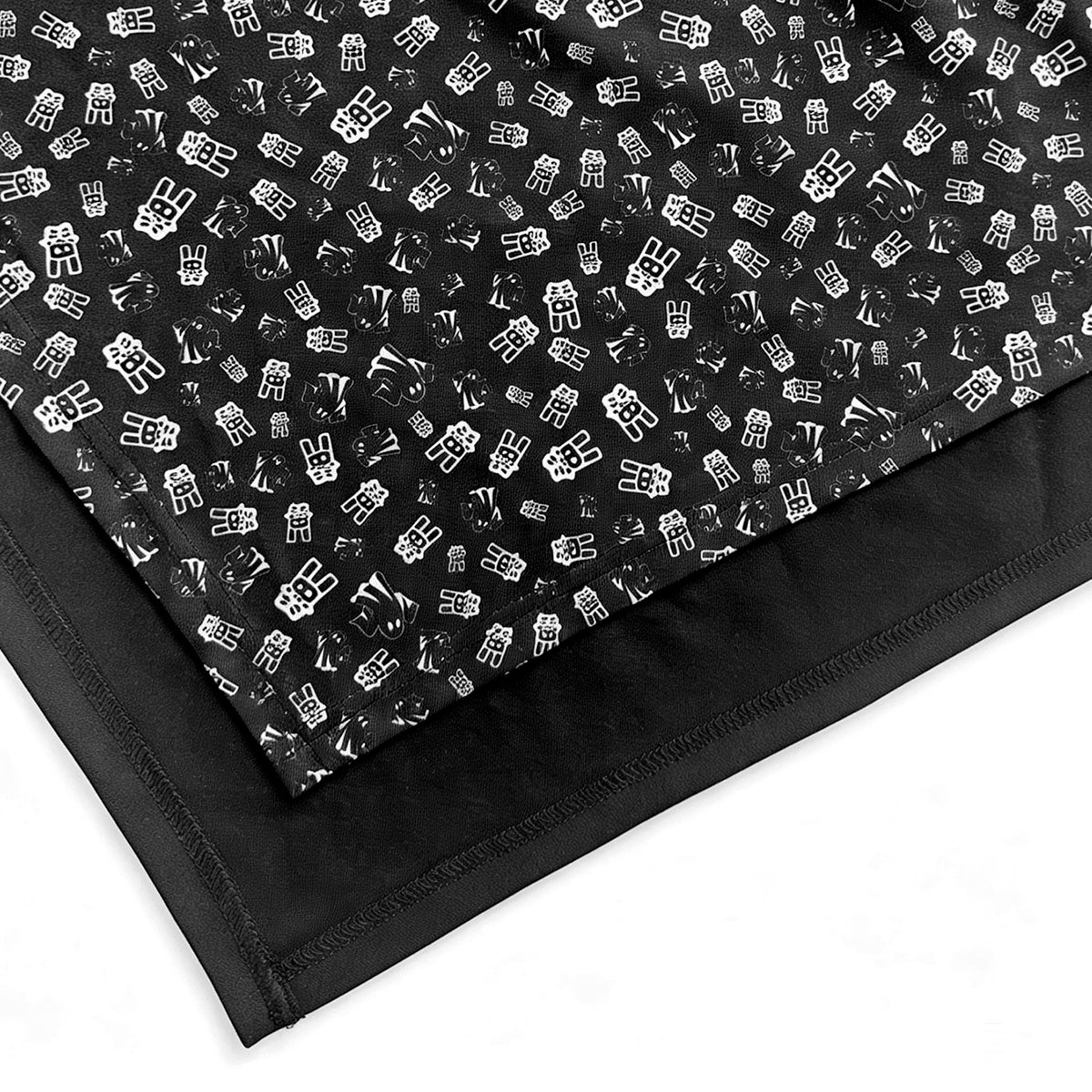 A close-up of a black blanket or quilt with a repeating white line-art pattern of small characters, folded over to show a solid black reverse side on a white background.
