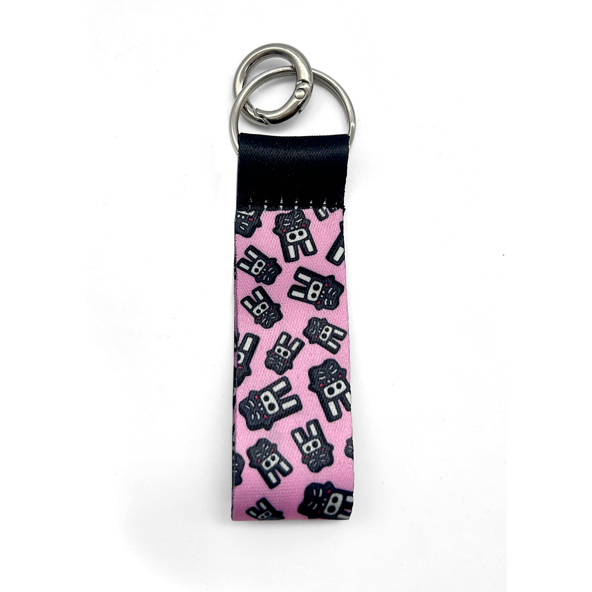 A pink fabric keychain strap featuring a repeating black cartoon character pattern, finished with a black stitched header and two silver metal key rings, shown on a white background.