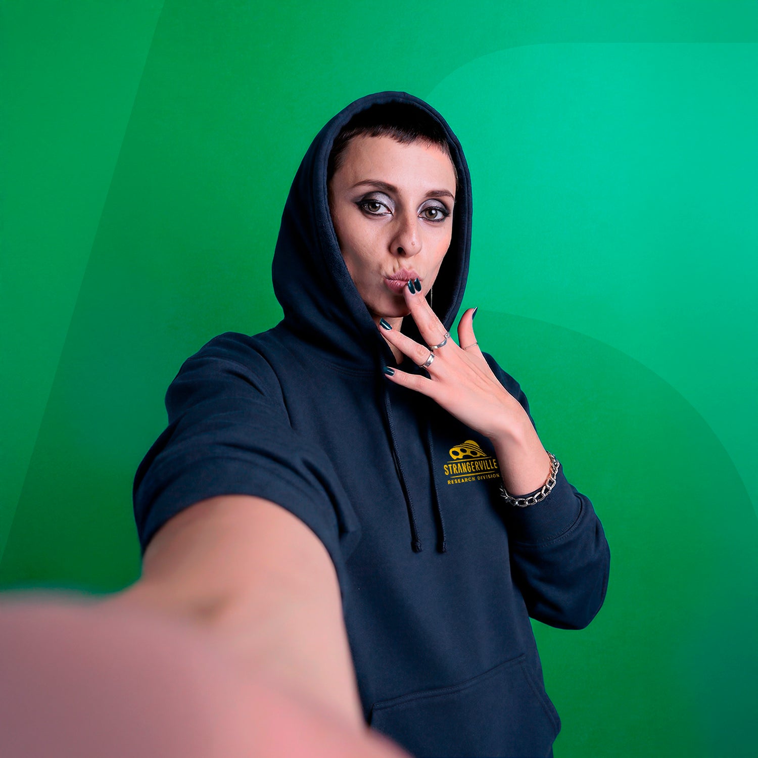 Person wearing a dark hoodie with a logo on a green background